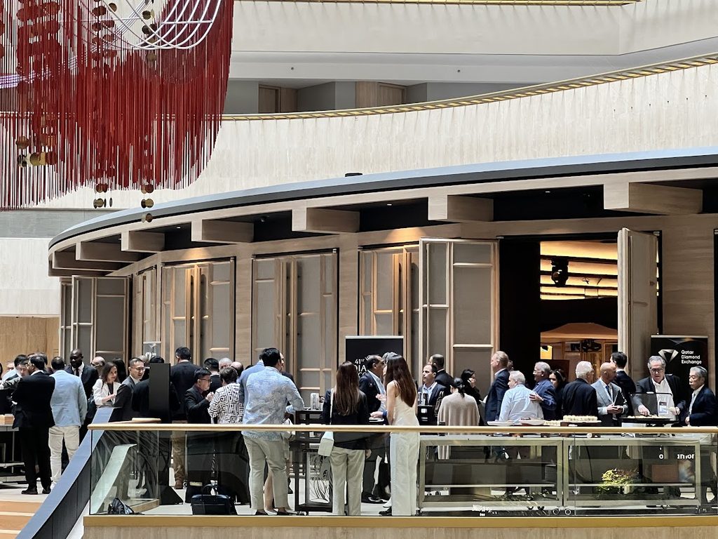 A wide shot of a hotel atrium with attendees networking near a curved wooden pavilion structure, red string lighting hanging overhead.